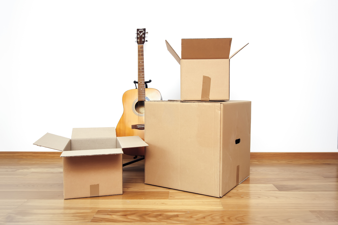 Open cardboard boxes with guitar on the floor in empty room, ready for transport