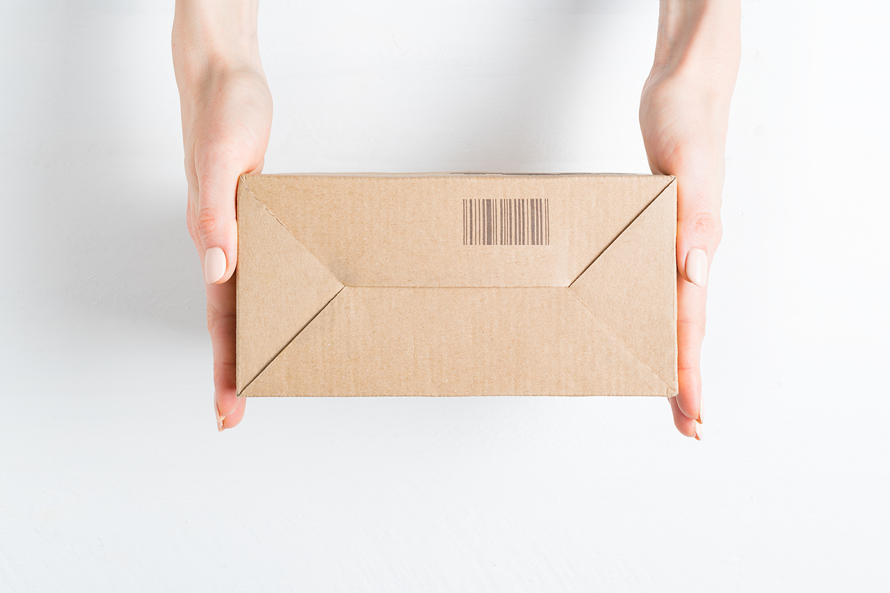 Rectangular cardboard box with barcode in female hands. Top view, white background