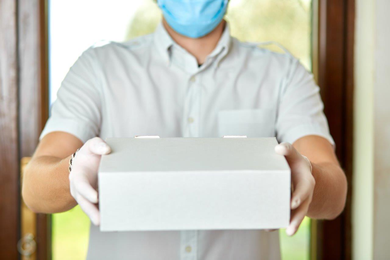 man wearing gloves and mask holding out package