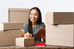 Small business owners, startup and e-commerce concept. Smiling successful asian businesswoman with own internet shop, selling online, writing shipping info on boxes with customer orders, use tablet